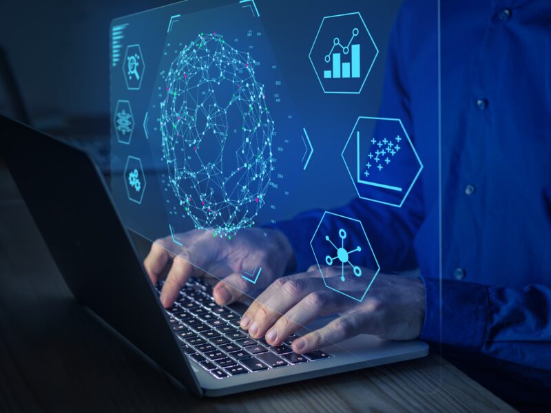 hands typing on laptop keyboard overlaid with blue graphics of graphs and icons