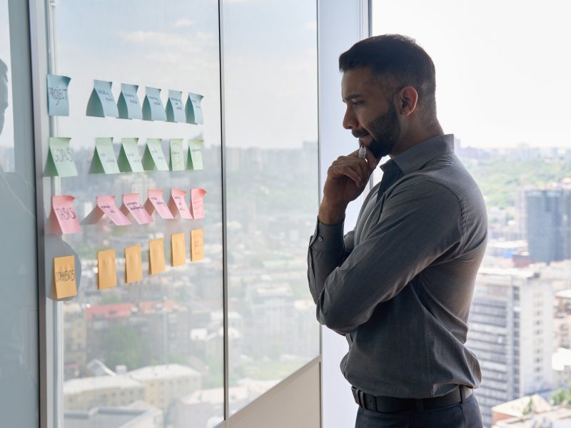 man thinking while looking at post-it notes on a glass wall