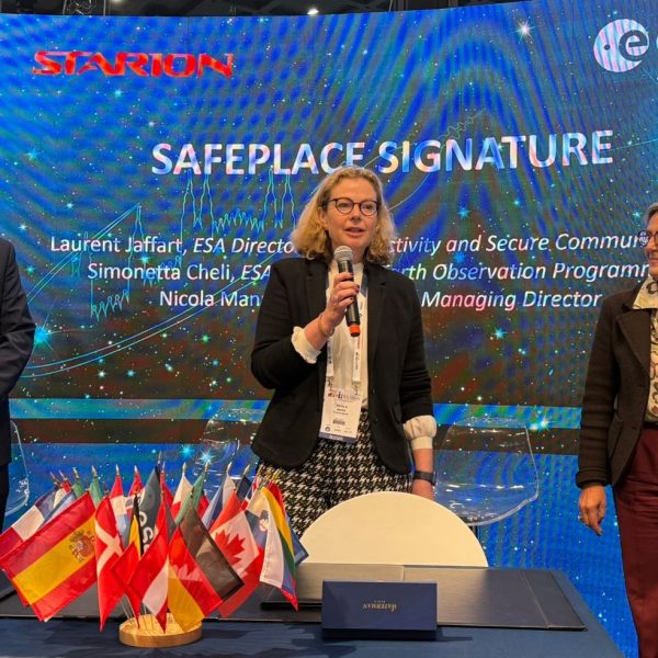 Signature event for the SAFEPLACE project at IAC2024 with Nicola Mann from Starion making a speech and a representative from ESA standing on either side of her in front of a large screen.