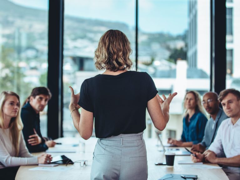 Back view of woman standing at table leading a team meeting